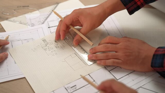 Professional engineer team discussion about house design on meeting table with architectural equipment and building blueprint scatter around at modern office. Focus on hand. Closeup. Delineation.