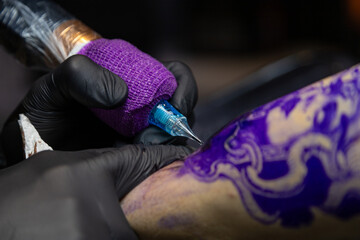 Close-up shot of a tattoo artist using a tattoo machine to create a detailed design on a client’s arm, with a focus on the purple stencil and black gloves. Perfect for tattoo art, creativity, and life