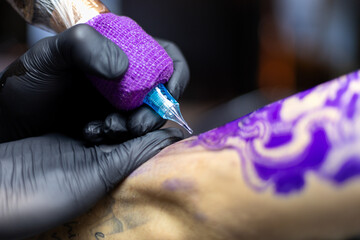 Close-up shot of a tattoo artist using a tattoo machine to create a detailed design on a client’s...
