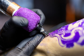 Close-up shot of a tattoo artist using a tattoo machine to create a detailed design on a client’s arm, with a focus on the purple stencil and black gloves. Perfect for tattoo art, creativity, and life