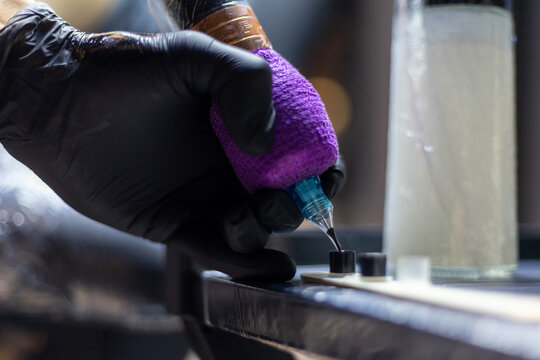 Close-up shot of a tattoo artist using a tattoo machine to create a detailed design on a client&rsquo;s arm, with a focus on the purple stencil and black gloves. Perfect for tattoo art, creativity, and life