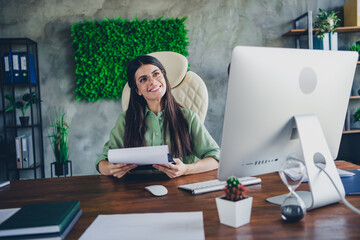 Confident young businesswoman with brunette hair in elegant formalwear working at desk in modern office