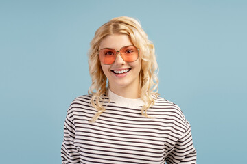 Fototapeta premium Smiling attractive stylish blonde girl wearing modern sunglasses, posing isolated on blue background