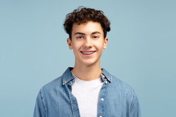 Portrait of smiling boy with dental braces wearing casual shirt isolated on blue background
