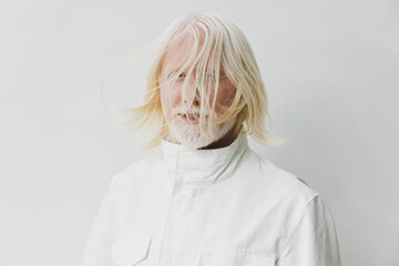 Mature man with long white hair, wearing a white jacket, standing against a light gray background,...