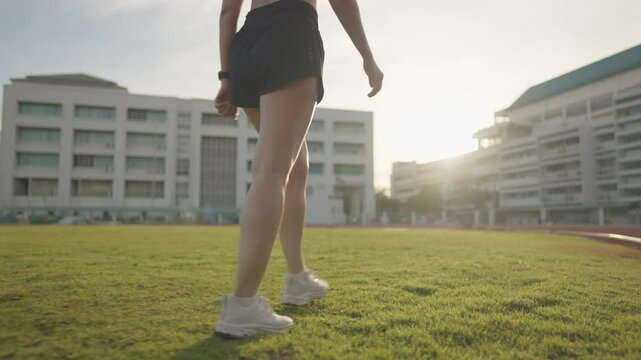 A woman is walking on a grassy field. The sky is clear and the sun is shining brightly. The woman is wearing a black shorts and a white top