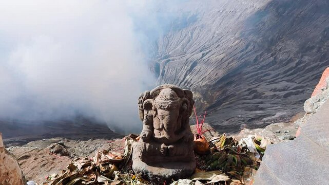 Ganesha statue on the top of Bromo volcano with a smoke rising fron crater in Java island Indonesia