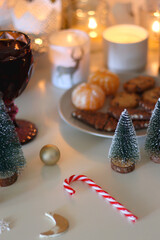 Various Christmas decorations, cookies, chocolate, nuts and tangerines, wine glasses and lit candles on the table. Holiday hygge at home. Selective focus.