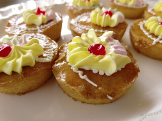Mini cakes coated with caramel and piped with whipped cream.