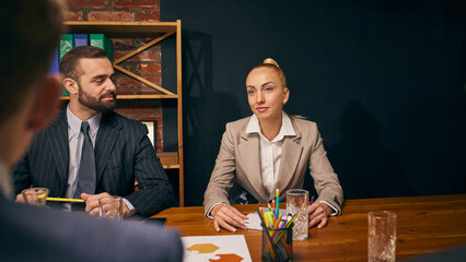 Businesswoman and businessman listen attentively during strategy session in modern office. Corporate meeting with colleagues. Concept of business, team strategy, collaboration, corporate discussion