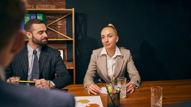 Businesswoman and businessman listen attentively during strategy session in modern office. Corporate meeting with colleagues. Concept of business, team strategy, collaboration, corporate discussion