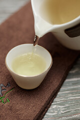 Gently pouring tea from a classic white teapot into a beautifully designed small cup