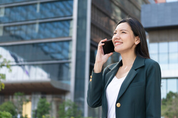 Asian senior businesswoman in green blazer smiles while talking on her phone outdoors. Women in Leadership,ceo