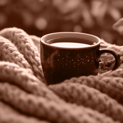 Mocha Mousse background Color of 2025 year. A Dark Mug with Tea or Coffee stands on a warm Blanket. A Hot Drink on a Cold Day. The Concept is a Lifestyle.