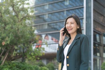 Asian senior businesswoman in green blazer smiles while talking on her phone outdoors. Women in Leadership,ceo,