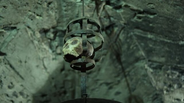 A chilling display of a human skull encased in an iron cage in a medieval dungeon tunnel. An evocative glimpse into historical torture practices.