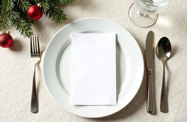  Mock up white card with a place for menu text lies on a white plate, cutlery and a glass lie nearby, the table is decorated with fir branches and a red ball, on a beige background