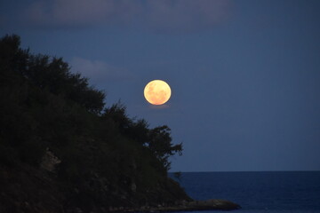 A bright orange full moon over an island in the Pacific ocean