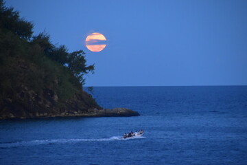 A bright orange full moon over an island in the Pacific ocean