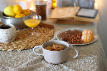 Books, e-reader, tea, orange juice, fruit, snacks, yarn, blanket and lit candles on the table....