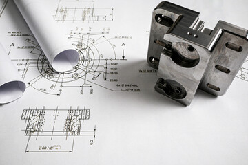 Metal part lying on engineering drawing with rolled blueprints, illustrating mechanical engineering...
