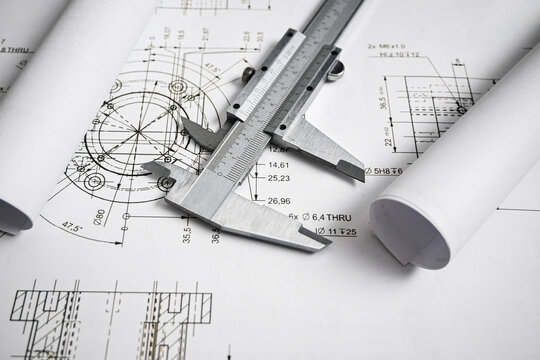 Caliper rests on rolled blueprints, highlighting the importance of precise measurements in engineering and design
