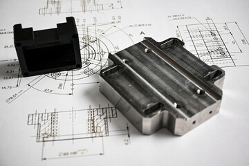 Plastic and metal prototypes are lying on a technical drawing with measurements, showcasing the process of product development