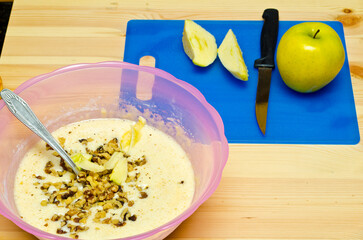 Making cookies. The cook has added walnut and starts to cut apple.