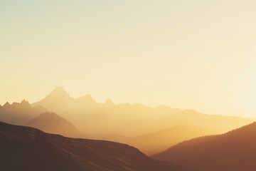 Mountain peak covered in snow illuminated by a warm sunrise, surrounded by layers of misty hills. 