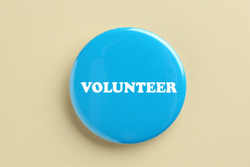 Button badge with word Volunteer on beige background, top view