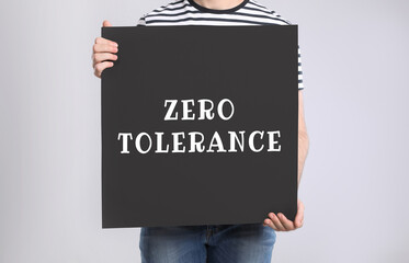 Man holding poster with words Zero Tolerance on light grey background, closeup