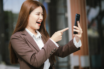 An Asian businesswoman works on her laptop in a trendy outdoor cafe in a bustling downtown area. She smiles confidently, projecting success.