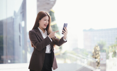 Fototapeta premium Confident Asian businesswoman standing on a busy city street with a smartphone in her hand, stylish and professional, representing the modern entrepreneur.