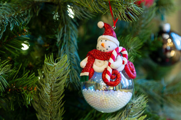 Selective focus view of cute snowman Christmas decoration hanging from artificial tree decorated...