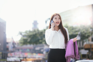 A businesswoman stands outdoors amidst a vibrant city, smiling while using her smartphone.