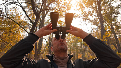 Amateur birdwatcher observing birds and other animals in nature with binoculars.
