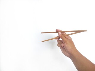 a hand holding a pair of wooden chopsticks against a plain white background. The focus is on the...