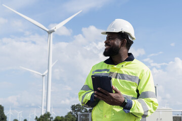 African American male engineer using digital tablet checking system of wind turbine at windmill field farm station. Male engineer monitoring and control windmill system at wind turbines station