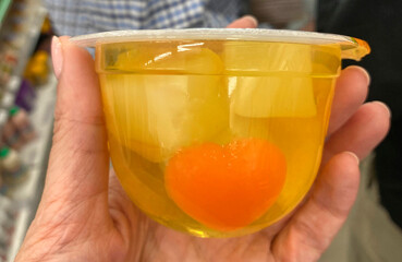 pieces of fruit in yellow jelly in a glass, in a girl's hand. Healthy snack, breakfast, Asian cuisine, food in Thailand