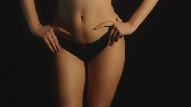 Closeup of a charming and seductive young woman in black underwear doing hip shake in a dark background.  