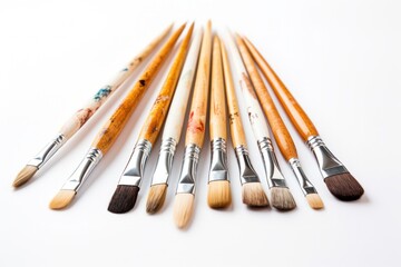 Fototapeta premium Close-up view of several paintbrushes with wooden handles and different bristle types, spread out in an organized manner on a white background