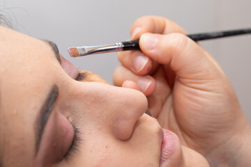 Beautician applying makeup on eyebrows with brush in beauty salon