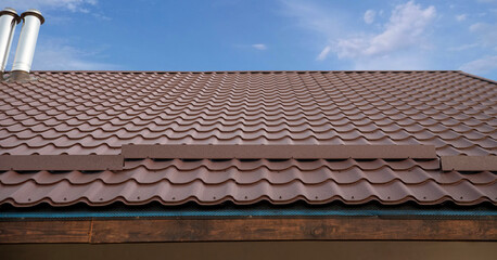 Brown metal snow guard installed on a corrugated tile roof.