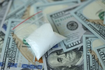 Small cocaine dose in plastic ziplock packet lies on big amount of american currency banknotes