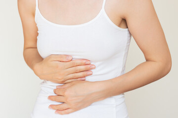 A young woman in white clothes holding her stomach with both hands, experiencing severe acute...
