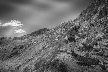 Young woman with sunglasses, long air and cap walking in the middle of dolomite peaks. Mount Latemar, Trentino, Italy. Traveling photography and outdoor sport activity concept. Black and white photo