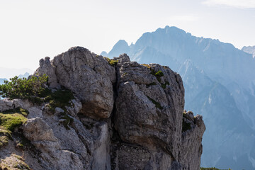 Obraz premium Unique rugged rock formation near mountain peak Jof di Miezegnot surrounded by majestic ridges of Julian Alps shrouded in misty haze, Friuli Venezia Giulia, Italy. Wanderlust in Italian Alps in summer
