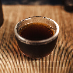 An Elegant Cup of Dark Tea beautifully placed on a Bamboo Mat, showcasing its charm
