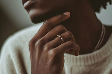 A hand adorned with a silver ring rests thoughtfully on a chin, illuminated by soft indoor light