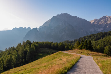 Winding hiking path through lush meadow with view of majestic mountains peaks Julian Alps in...